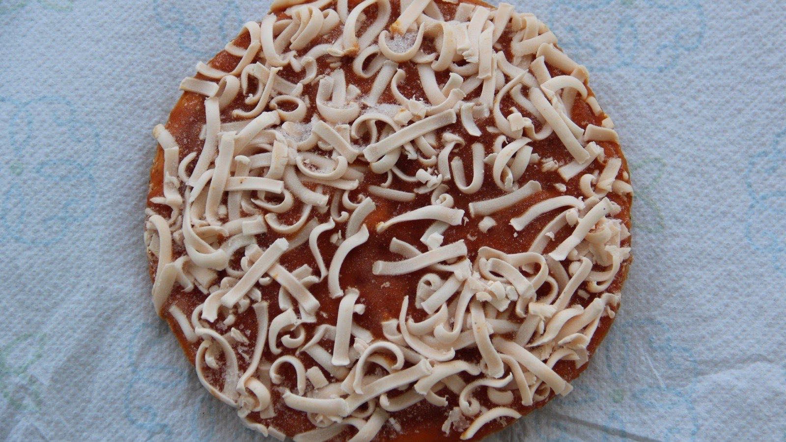 An uncooked frozen personal pizza, its sauce covered in pale shredded cheese that has not been melted.